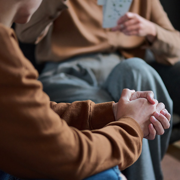 A closeup of two people in a therapy-style meeting, focusing on one person's clasped hands