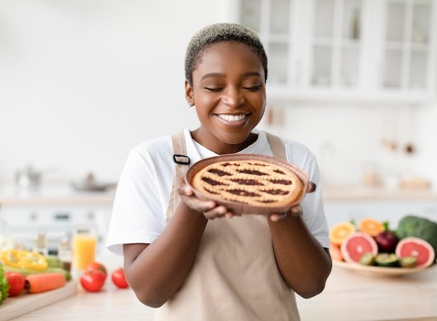 Smiling young African-American woman in apron admiring a freshly baked pie