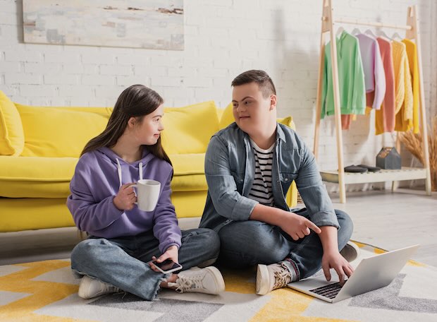 Teen boy with Down syndrome pointing at a laptop near friend holding a cup